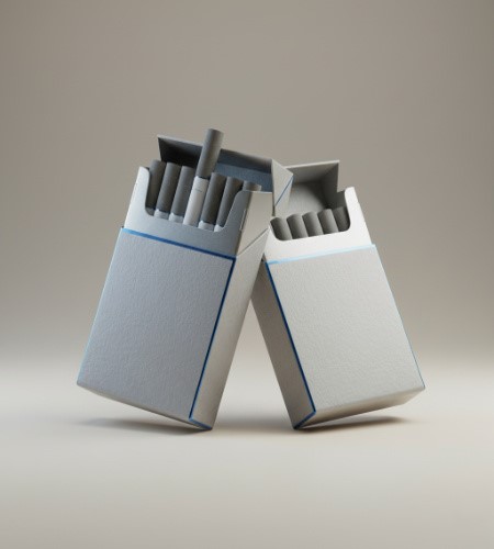 Two minimalist light-grey cigarette packs with thin blue borders lean against each other on a neutral surface. Both packs are open, revealing cigarettes with dark grey filters, with one cigarette slightly elevated in the pack on the left.